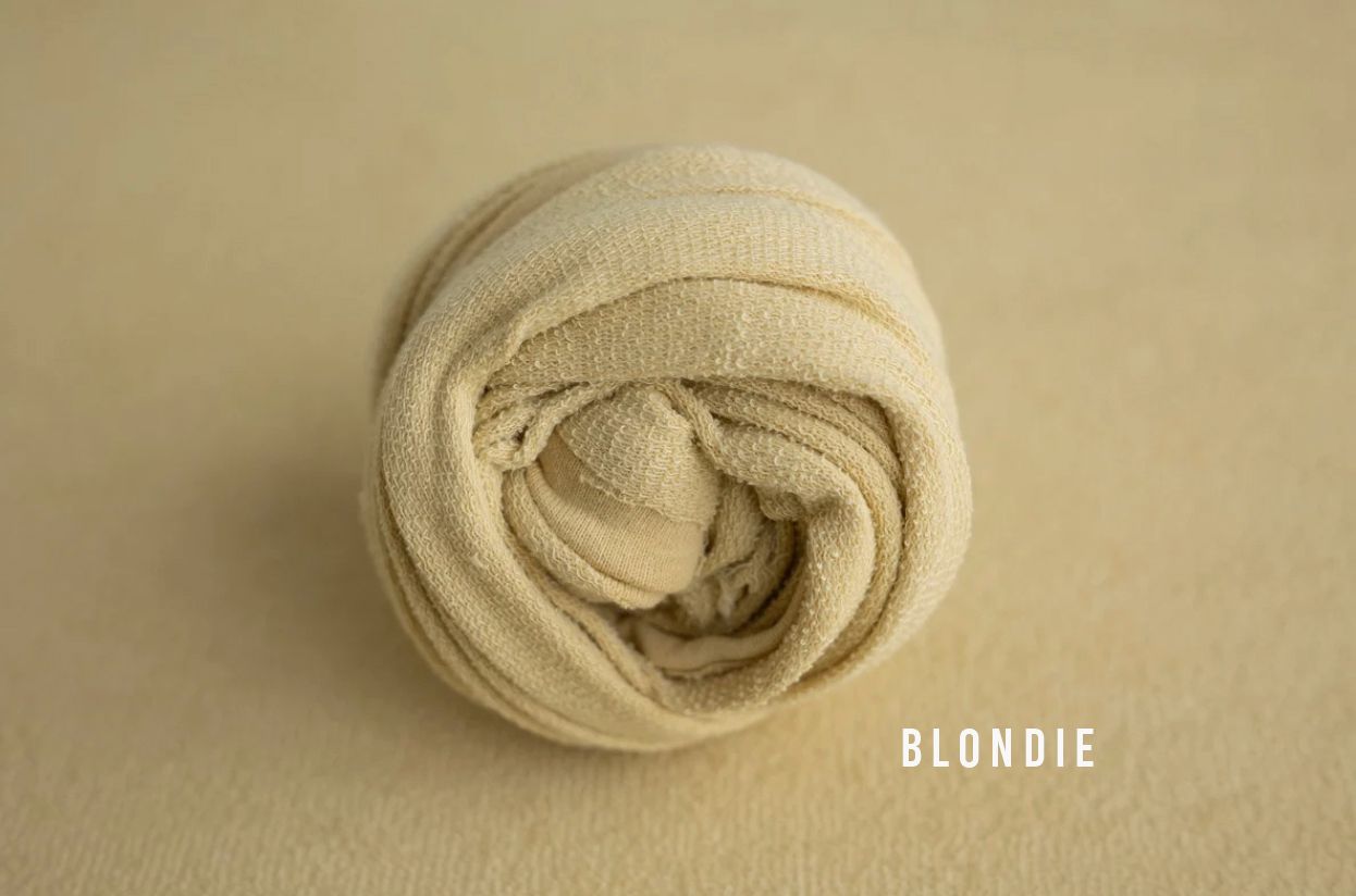 Blondie cream ivory knit stretch wrap rolled neatly for newborn photography props on a soft beige background.