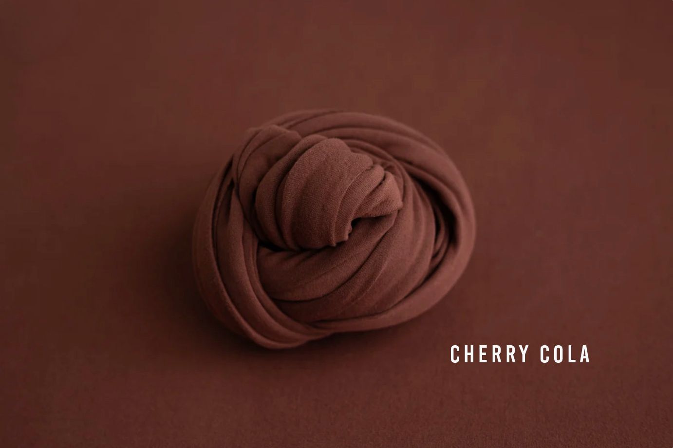 Cherry Cola brown newborn wrap fabric coiled on a matching dark brown background for photography props.