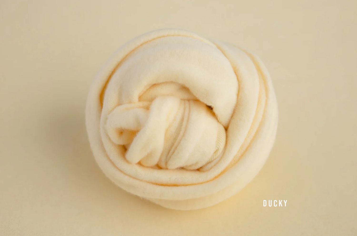 A soft white dough ball shaped into an elegant swirled knot on a cream background.