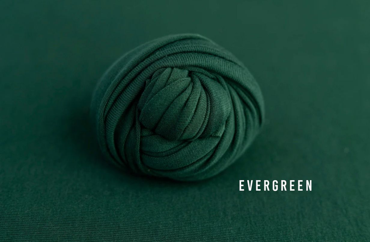 Evergreen dark green fabric wrap rolled into a ball on a matching green background for newborn photography.