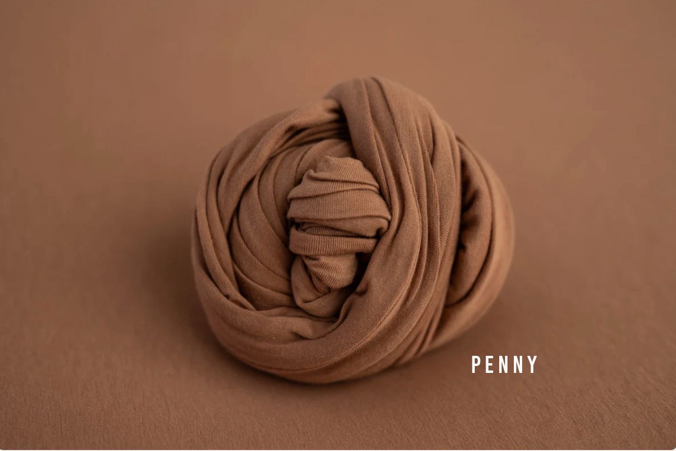 Penny brown stretch fabric wrap coiled into a bundle on a warm brown background for newborn photography.