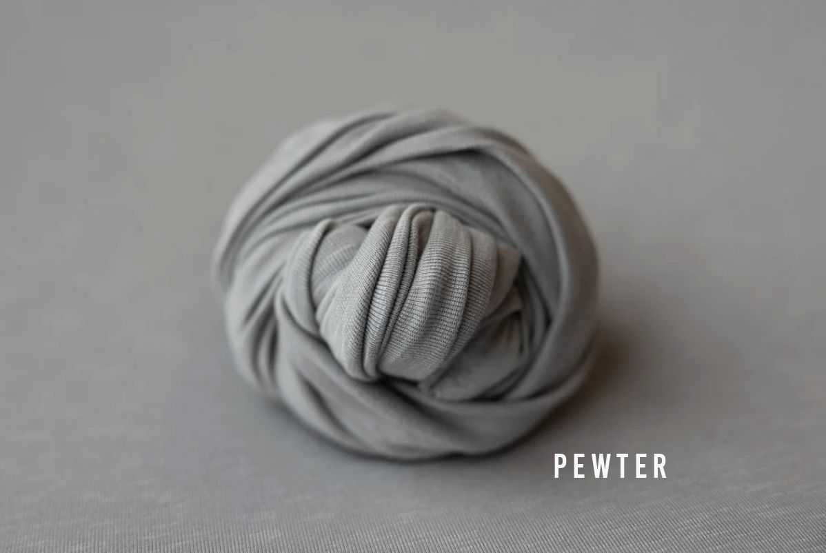 Pewter light gray fabric wrap coiled into a neat ball on a soft gray background for newborn photography.
