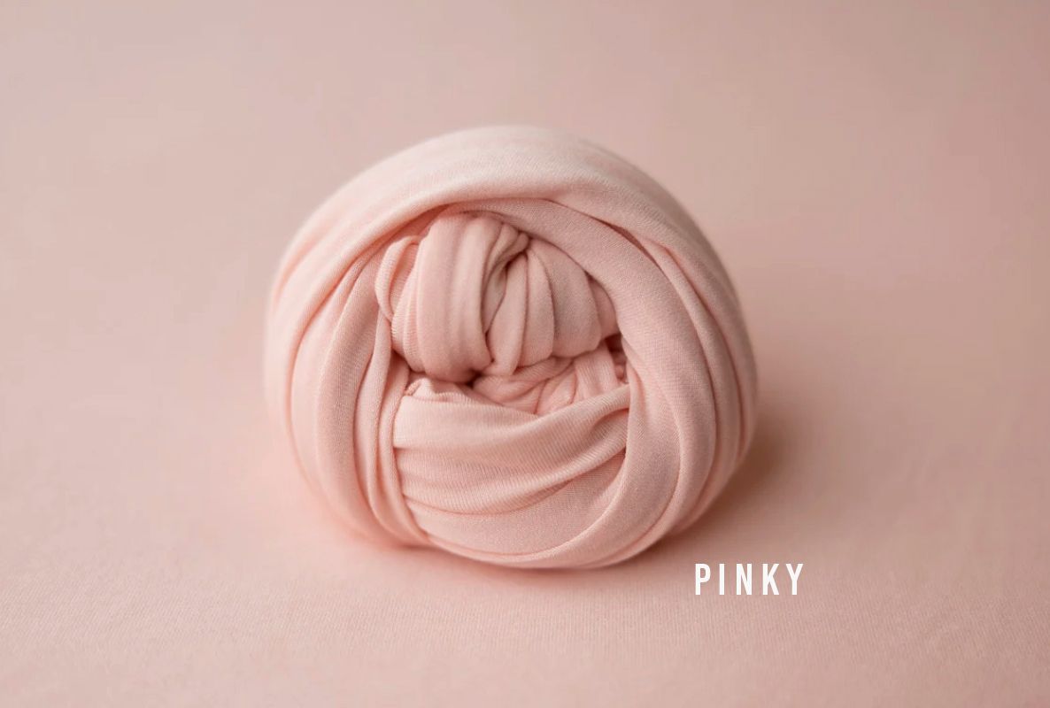 Soft pink newborn photography wrap neatly rolled, labeled Pinky, on a matching blush pink background.