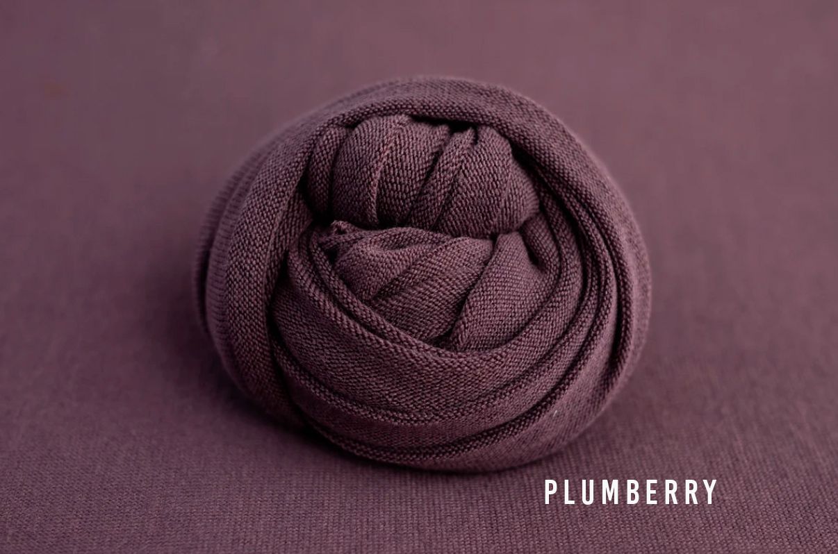 Plumberry deep purple fabric wrap coiled into a ball on a matching plum background for newborn photography.
