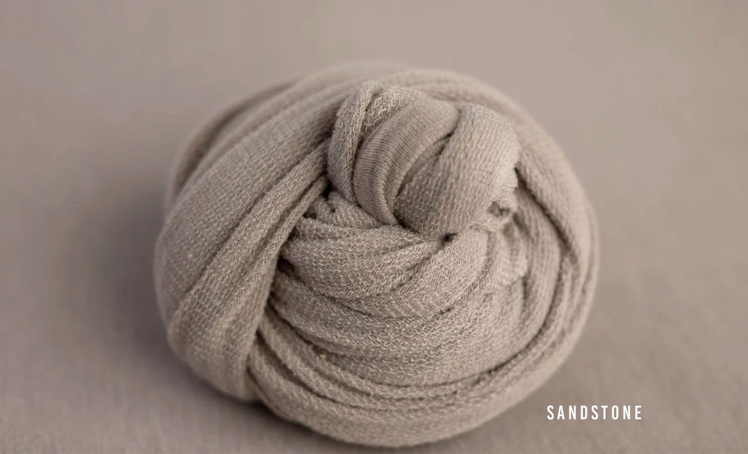Sandstone beige knit wrap coiled into a round bundle for newborn photography props.