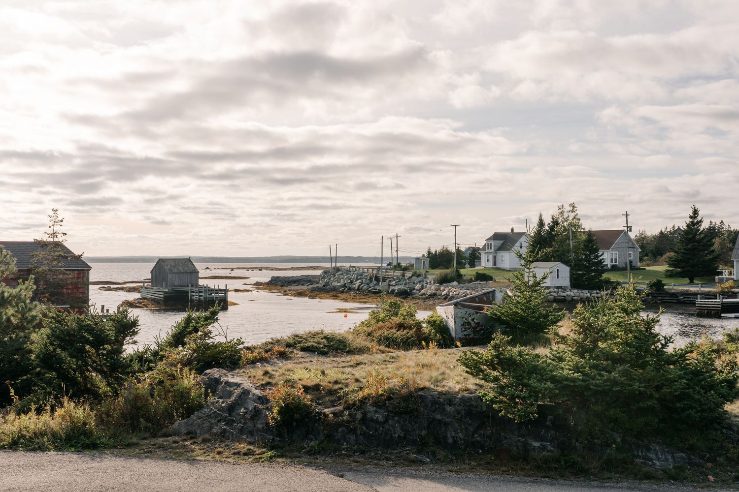 Coastal fishing village with rocky shoreline, small wooden buildings, and overcast sky in Nova Scotia, Canada.