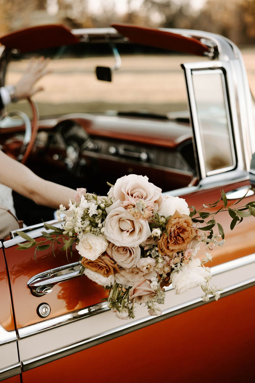 Bridal bouquet of blush and rust roses resting on a vintage copper convertible car door.