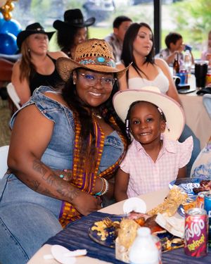 Woman and young girl wearing cowboy hats smile together at a western-themed birthday party celebration.