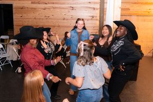 Group of people in cowboy hats line dancing and socializing at a country western themed indoor party event.