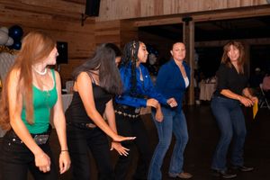 Women line dancing in a rustic barn venue at a country western themed party with balloon decorations.