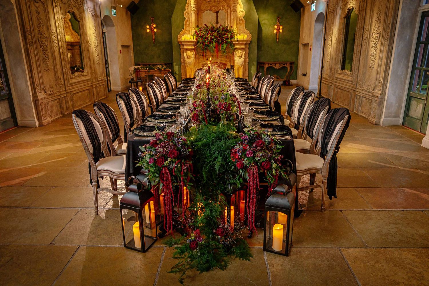 Long black banquet table with red flowers and candle lanterns in the Le Petit Chateau ceremony room set for a gothic wedding breakfast
