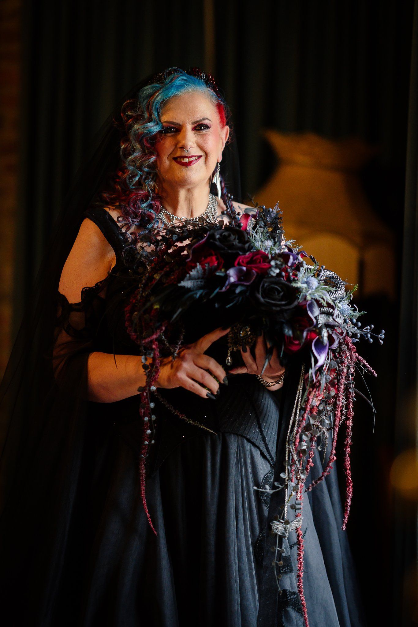 Portrait of a bride in a black wedding dress and veil holding a cascading dark red and purple bouquet