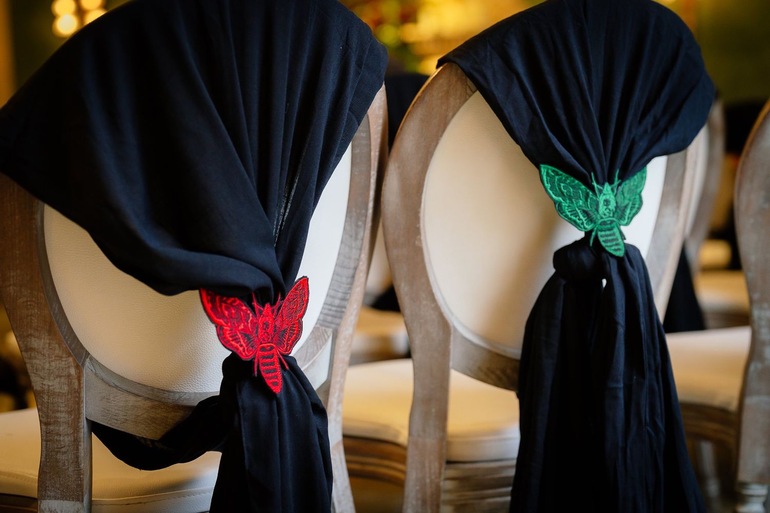 Black chair covers tied with red and green embroidered moths by Romantic Outlaw at a Halloween themed wedding