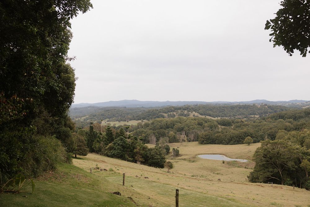 Rolling green pastoral hills with a small farm pond, scattered trees and distant forested ridges under an overcast sky.