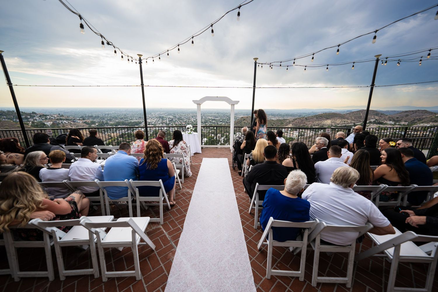 Outdoor wedding ceremony aisle with a white arch and seated guests.