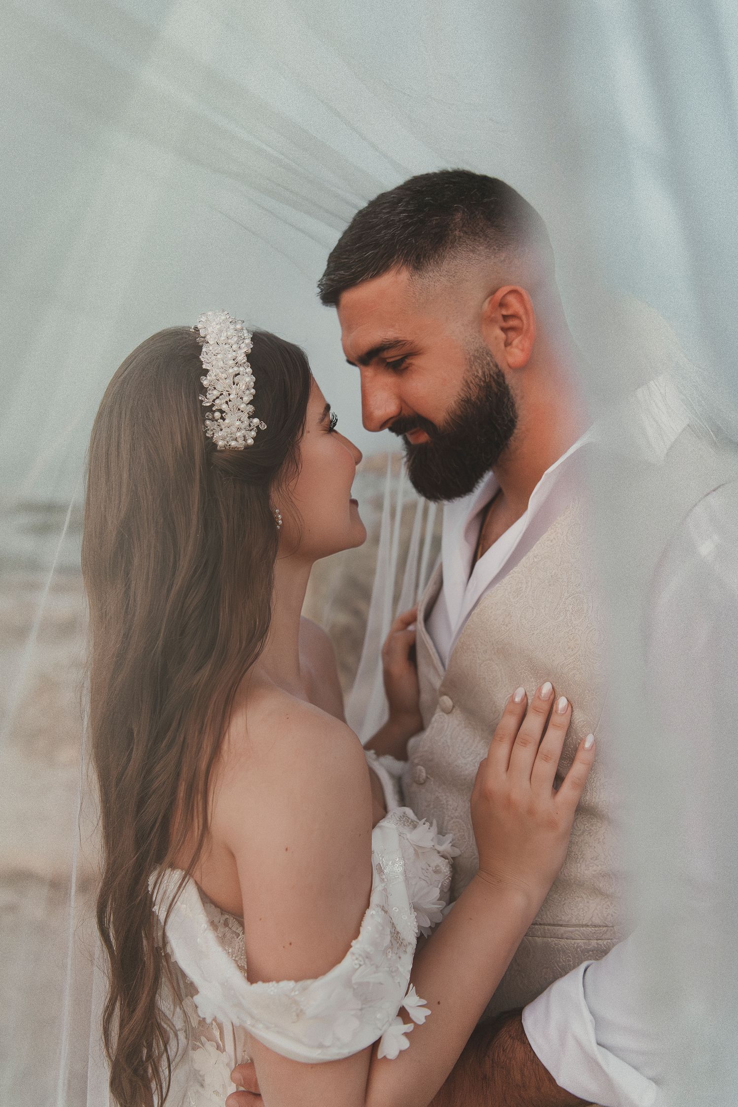Cinematic wedding photography featuring a close-up portrait of the bride and groom framed by a soft tulle veil.