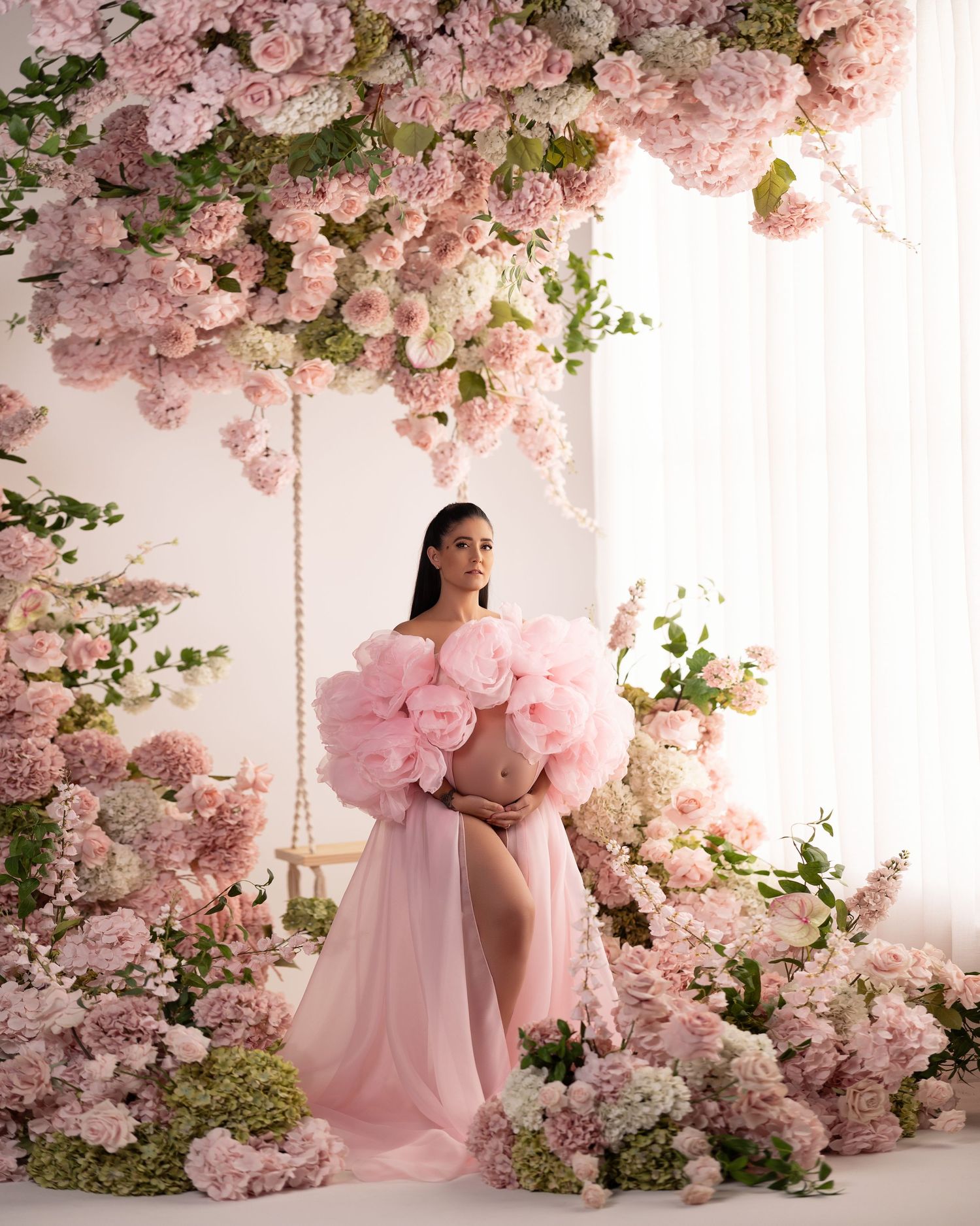 A dreamy maternity photoshoot setup with cascading pink floral arrangements and soft romantic lighting.