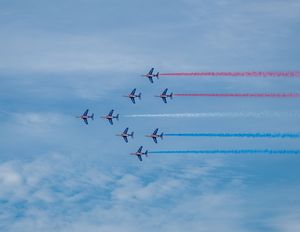 Nine jets in formation trail red, white, and blue smoke across a partly cloudy sky in a precision aerobatic airshow display.