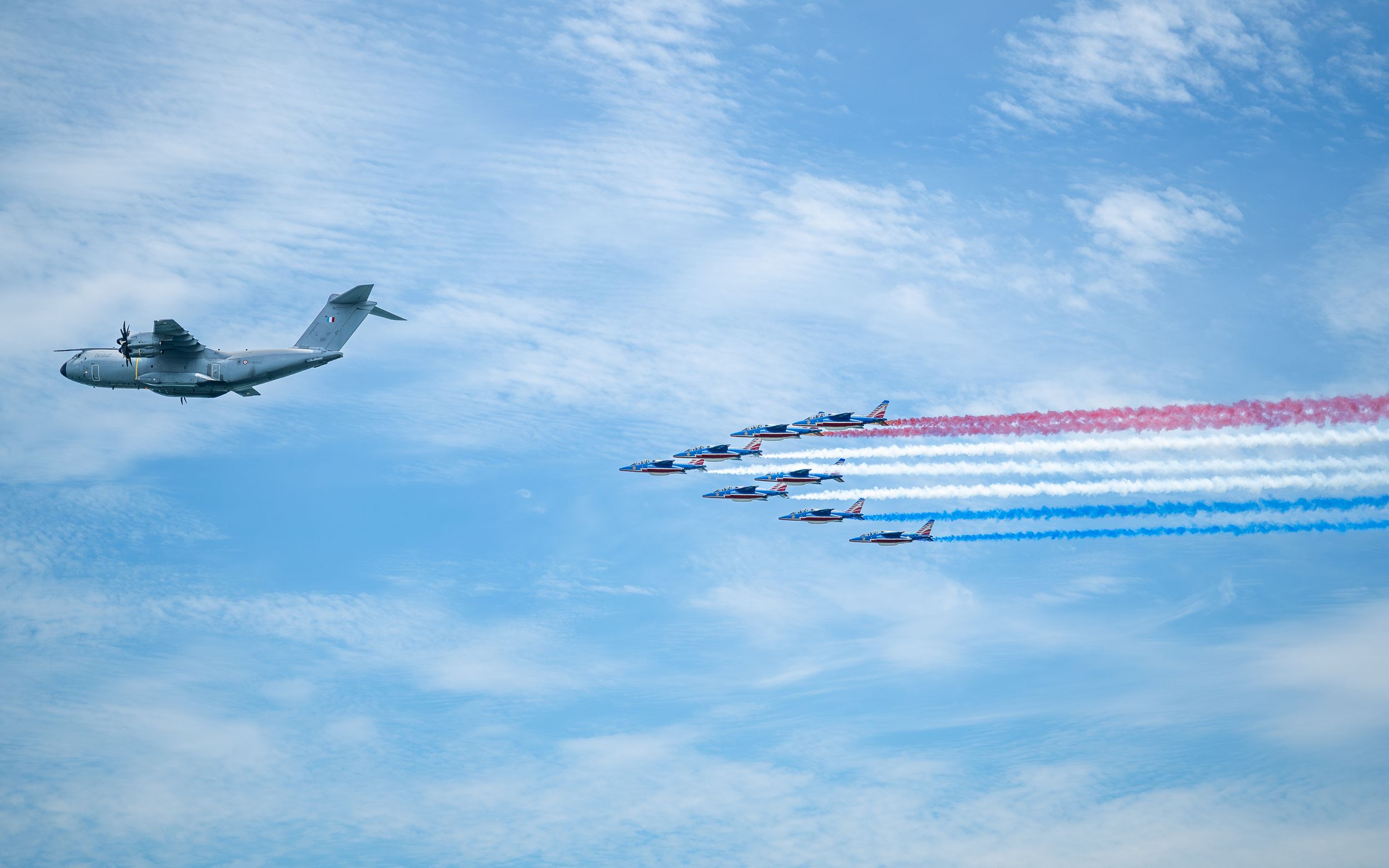 Military airshow featuring an A400M transport aircraft alongside jets trailing red, white, and blue smoke against a blue sky.