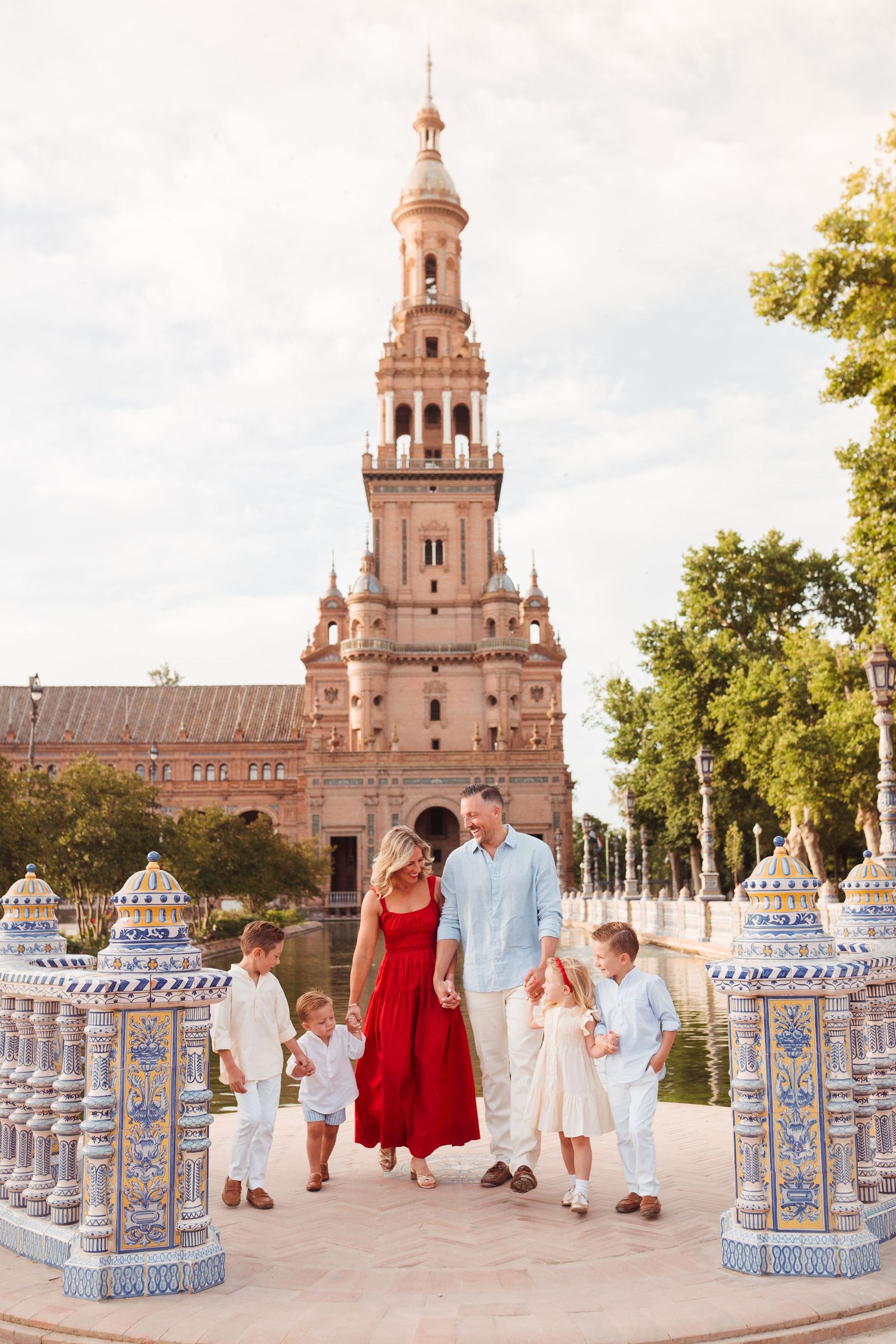 Family with children walking at Plaza de Espana in Seville, Spain, with ornate tower and blue tile columns.