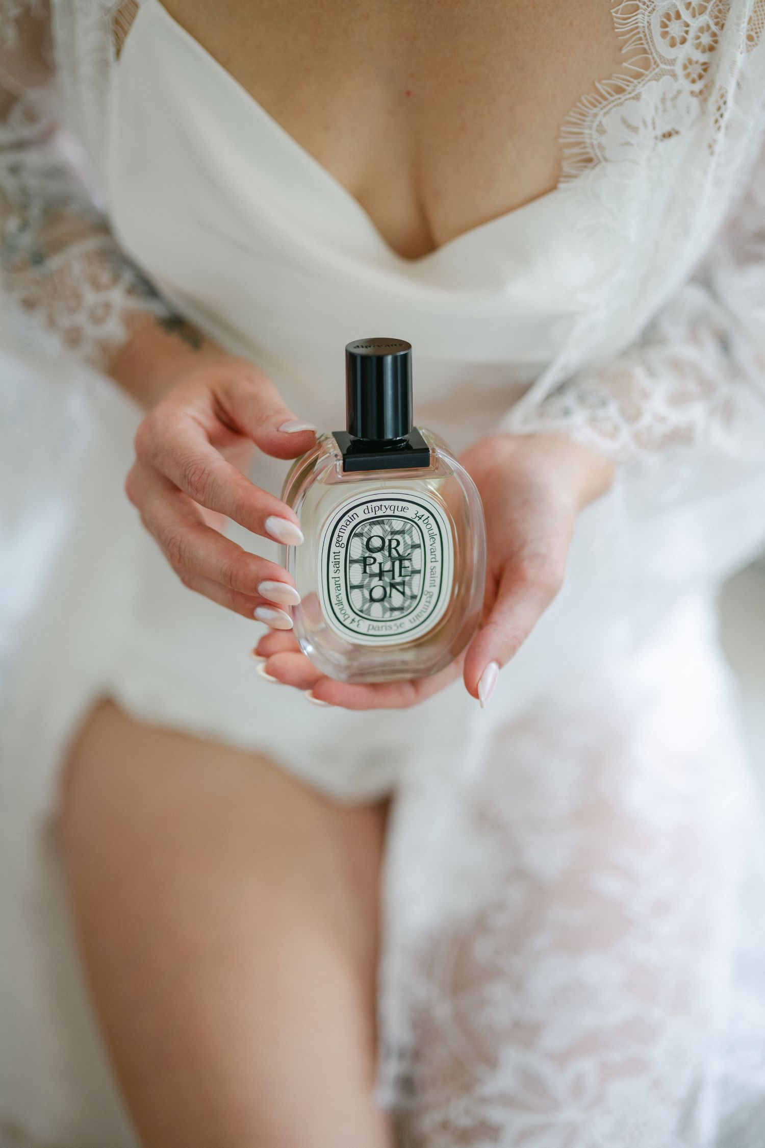 Smiling bride in white lace robe holding her wedding dress, preparing for her special day indoors.