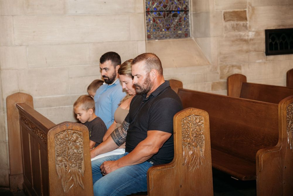 Family sitting together in wooden church pews during a service inside a stone chapel.