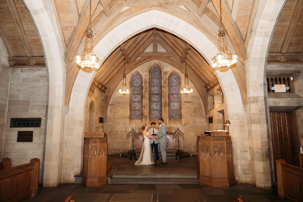 Bride and groom exchange vows at the altar of a stunning Gothic stone church with arched ceilings and stained glass windows.