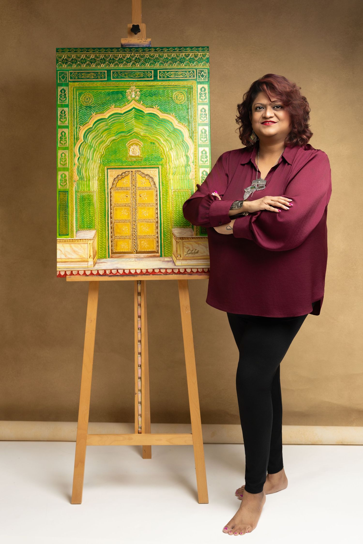 Artist standing beside a vibrant green Indian architectural painting on an easel, wearing a maroon shirt.