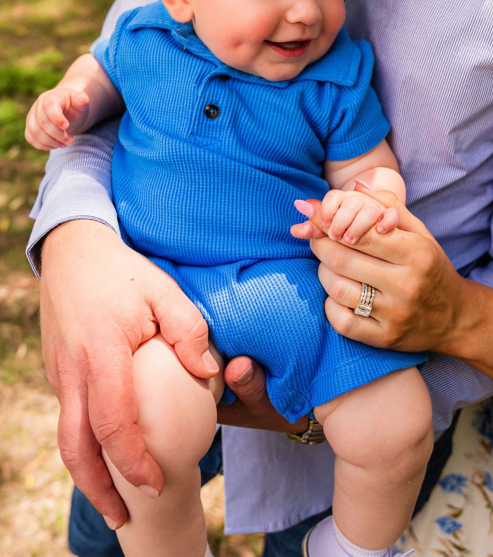 Happy baby in blue romper being held by parents outdoors during a family photo session.
