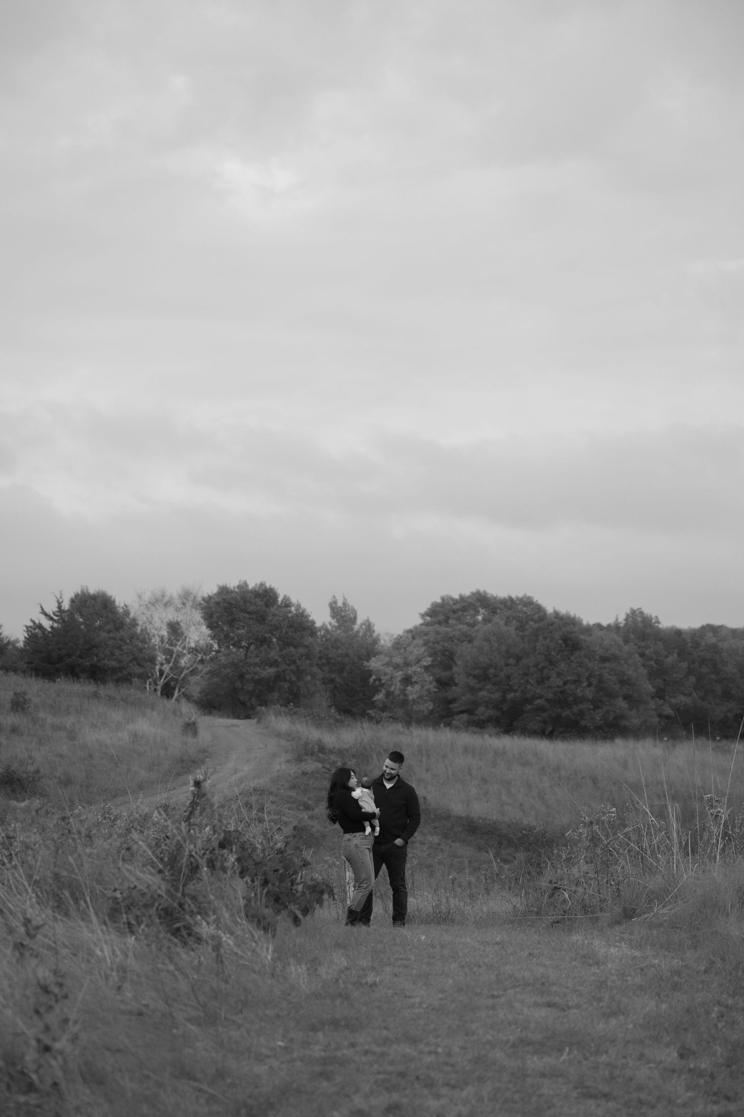 a candid photo of mom and dad holding their infant with rolling hills scenery during fall mini session in hudson wisconsin
