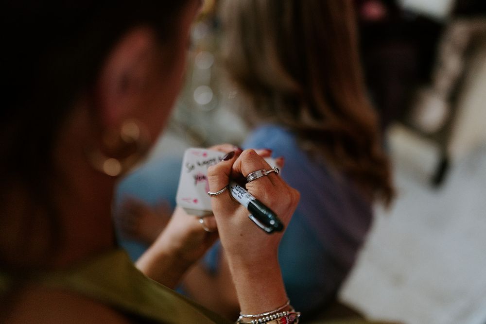 Close-up of a woman's hands adorned with multiple rings and bracelets, holding a small white cup at a social gathering.