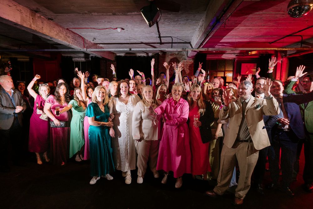 A joyful crowd of elegantly dressed guests celebrating with raised arms on a colorful dance floor at a festive event.