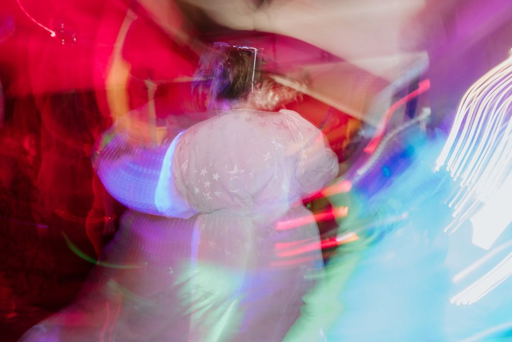 Blurred motion photo of a DJ performing under colorful neon lights at a vibrant nightclub event.