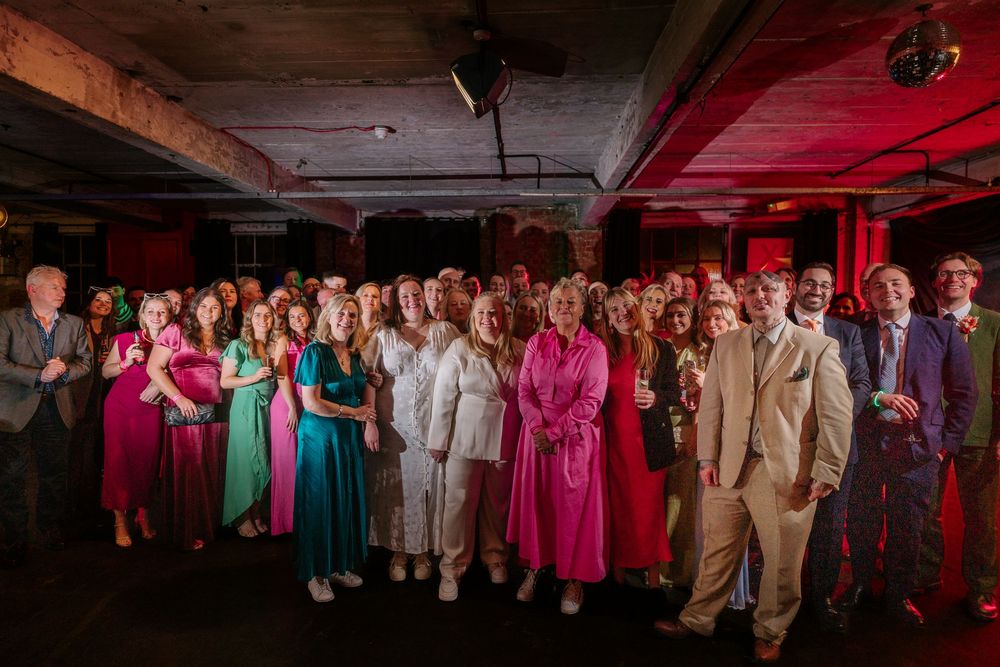 Large group of elegantly dressed guests posing together at a vibrant indoor event with red ambient lighting.