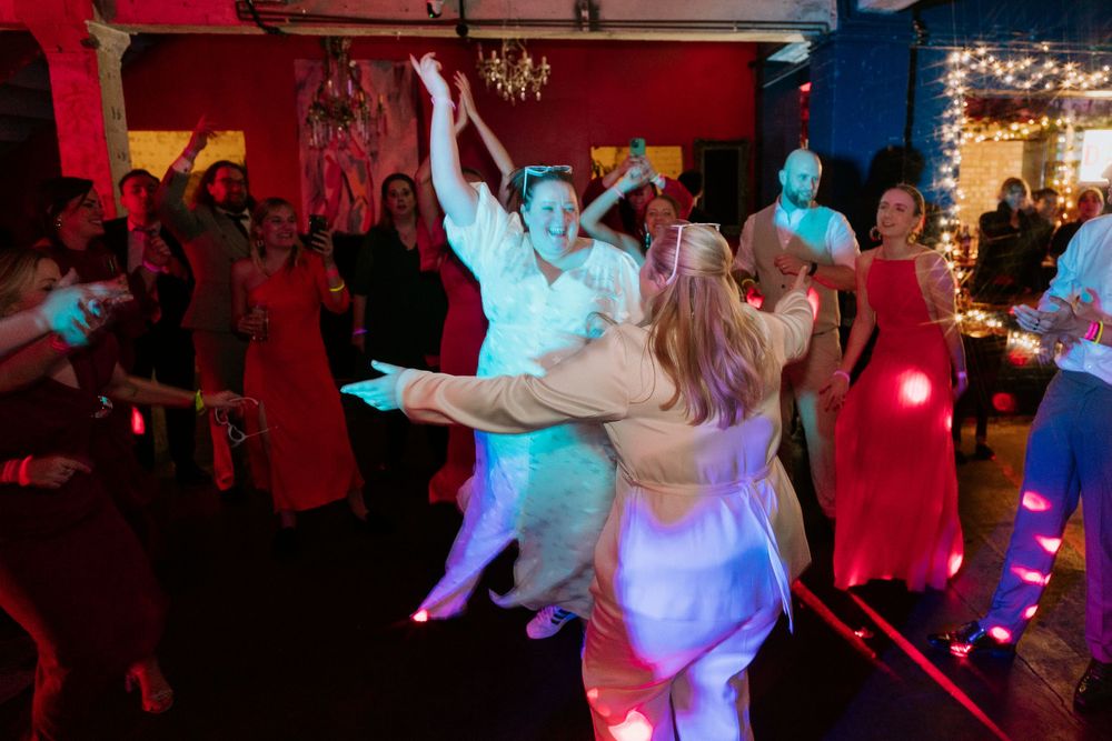 Guests dancing joyfully at a wedding reception in a vibrant venue with colorful lights.