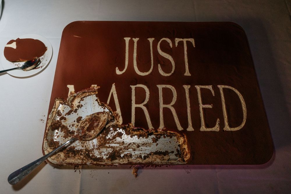 A partially cut Just Married chocolate wedding cake with white frosting on a white tablecloth.