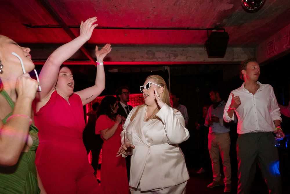 Group of guests dancing at a wedding reception under red lights.