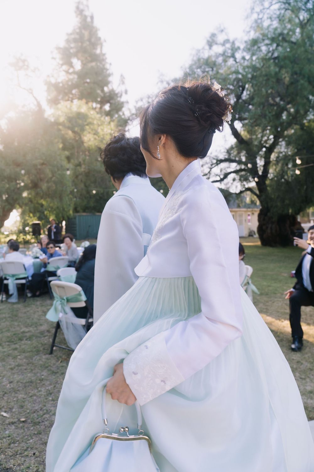 Woman in traditional Korean hanbok dress at an outdoor wedding ceremony on a sunny day.