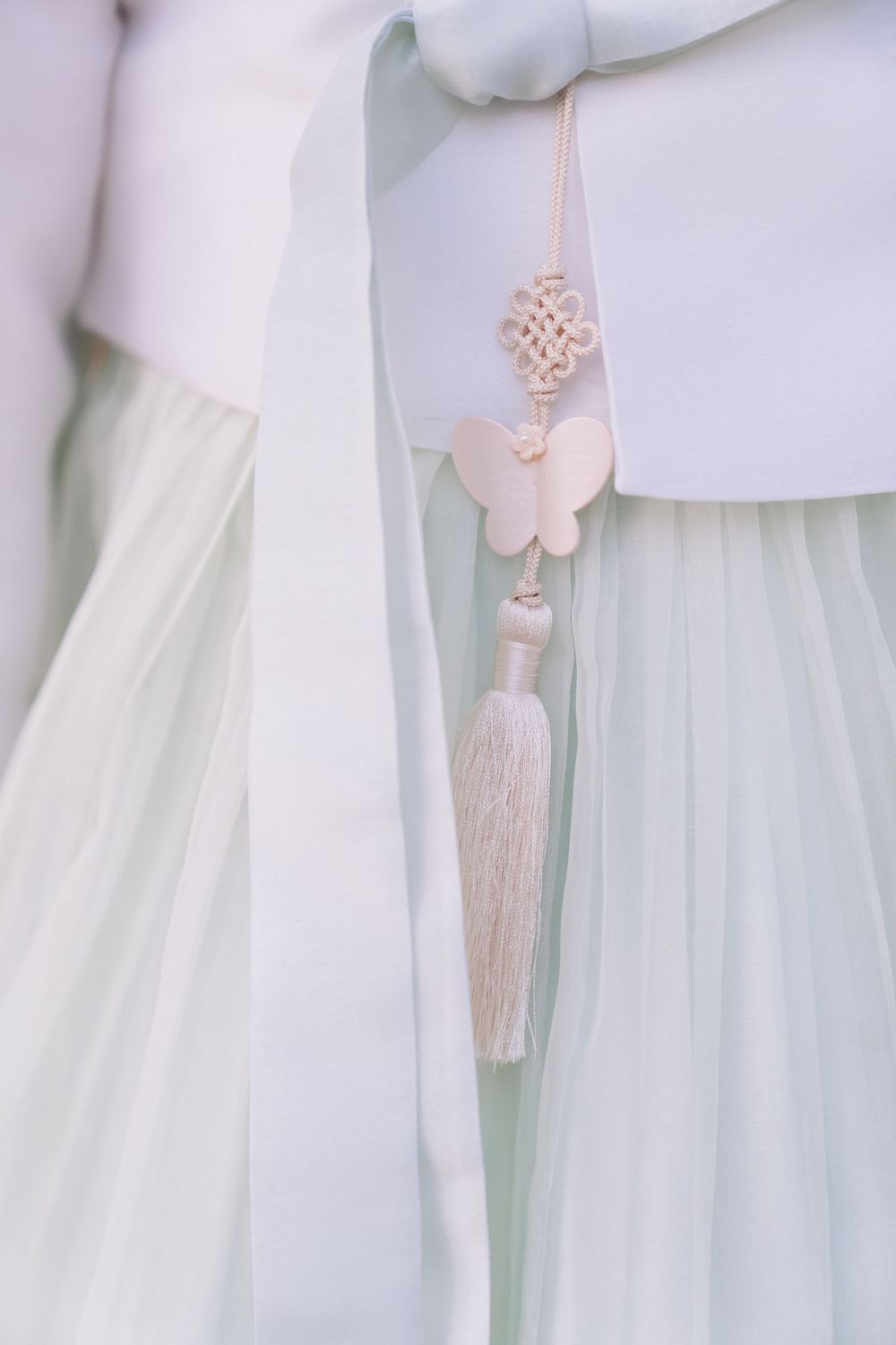 Elegant Korean hanbok detail with mint tulle skirt, white top, and blush butterfly tassel ornament.