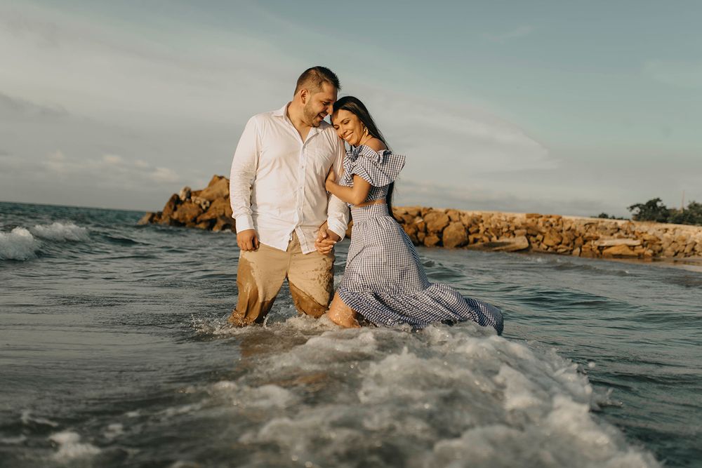 Romantic couple walking hand in hand through ocean waves on a tropical beach at golden hour.