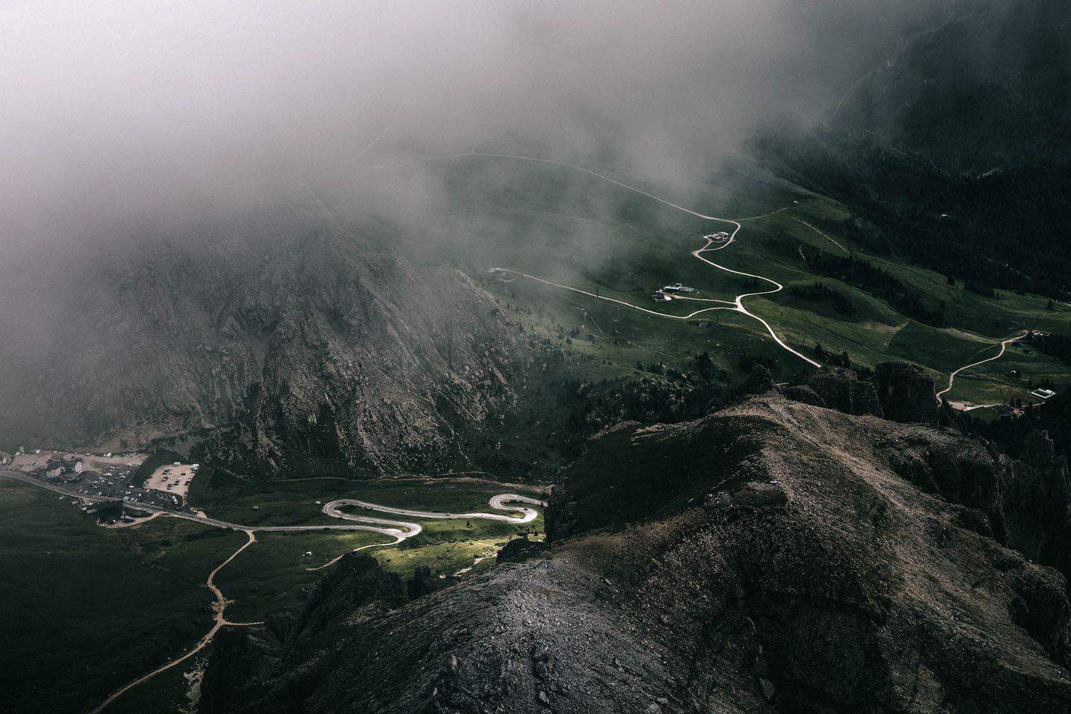 Dramatic Dolomite mountains with jagged rocky peaks, winding road, and moody overcast sky in the Italian Alps.