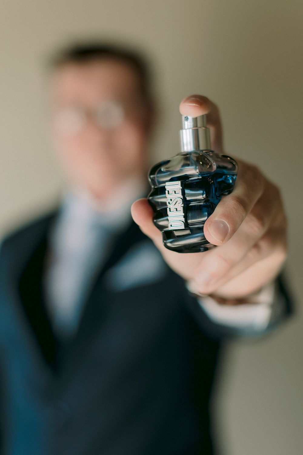 Man in suit holding Diesel cologne bottle toward camera in close-up shot.
