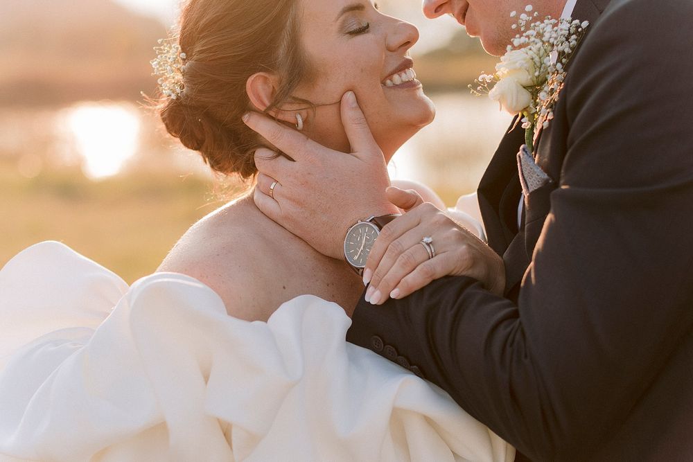 Bride and groom share a tender moment at golden hour, with groom cradling bride's face as she laughs joyfully.
