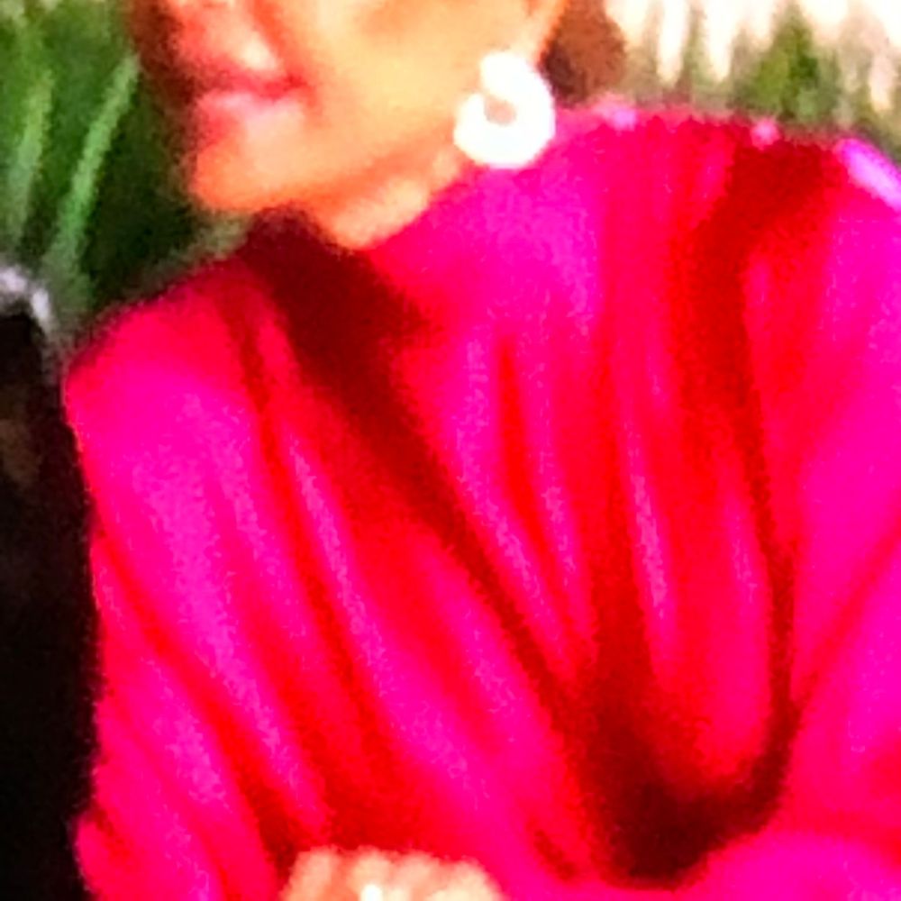 A woman wearing a bright red turtleneck sweater and white hoop earrings poses for a photo.