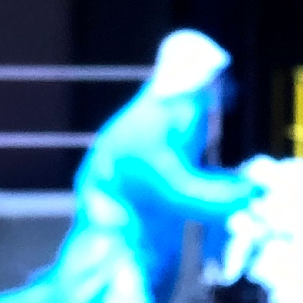 Glowing cyan blue silhouette of a hooded figure on a dark stage.