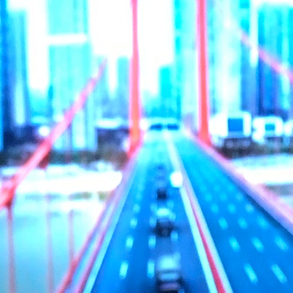 Aerial view of a modern city highway bridge with red cables and urban skyline.