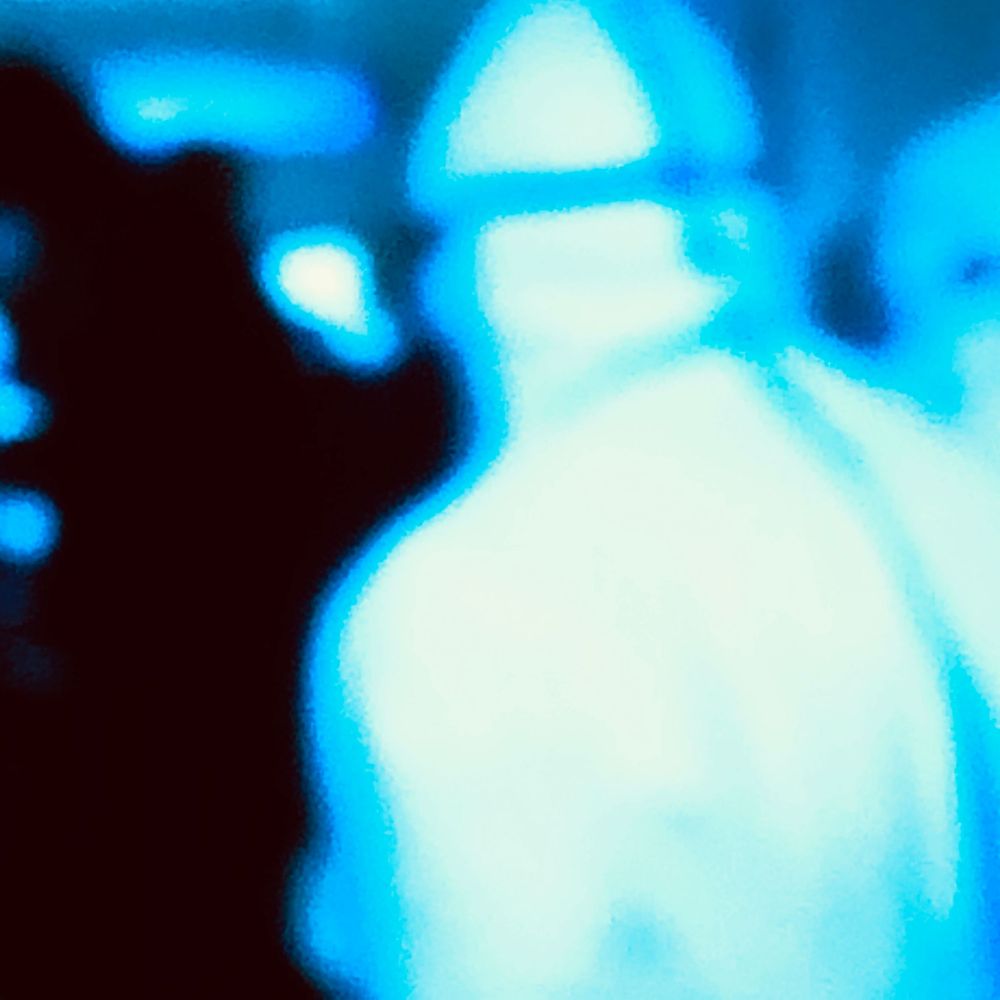 Glowing blue thermal or infrared silhouette of a person wearing a cap in a dark environment.