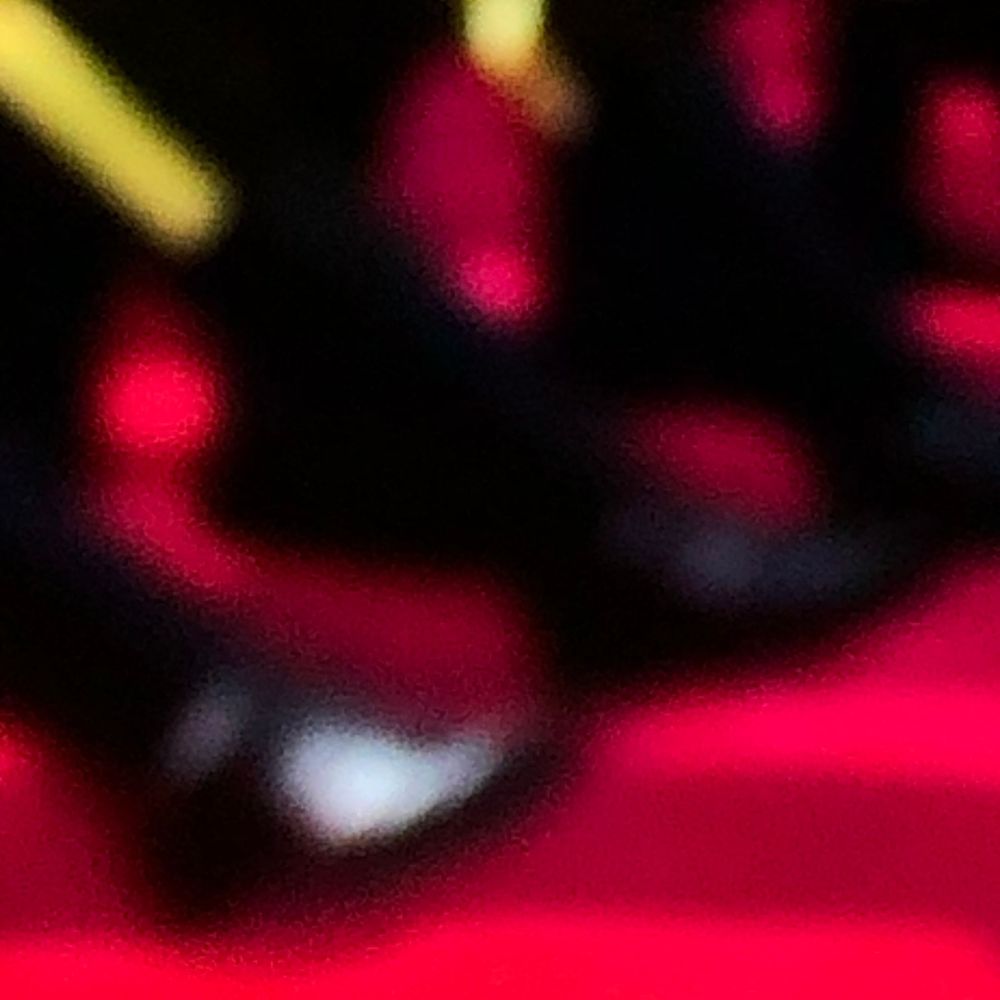 Blurry close-up of black high heels on a vibrant red surface with bokeh lighting effects.