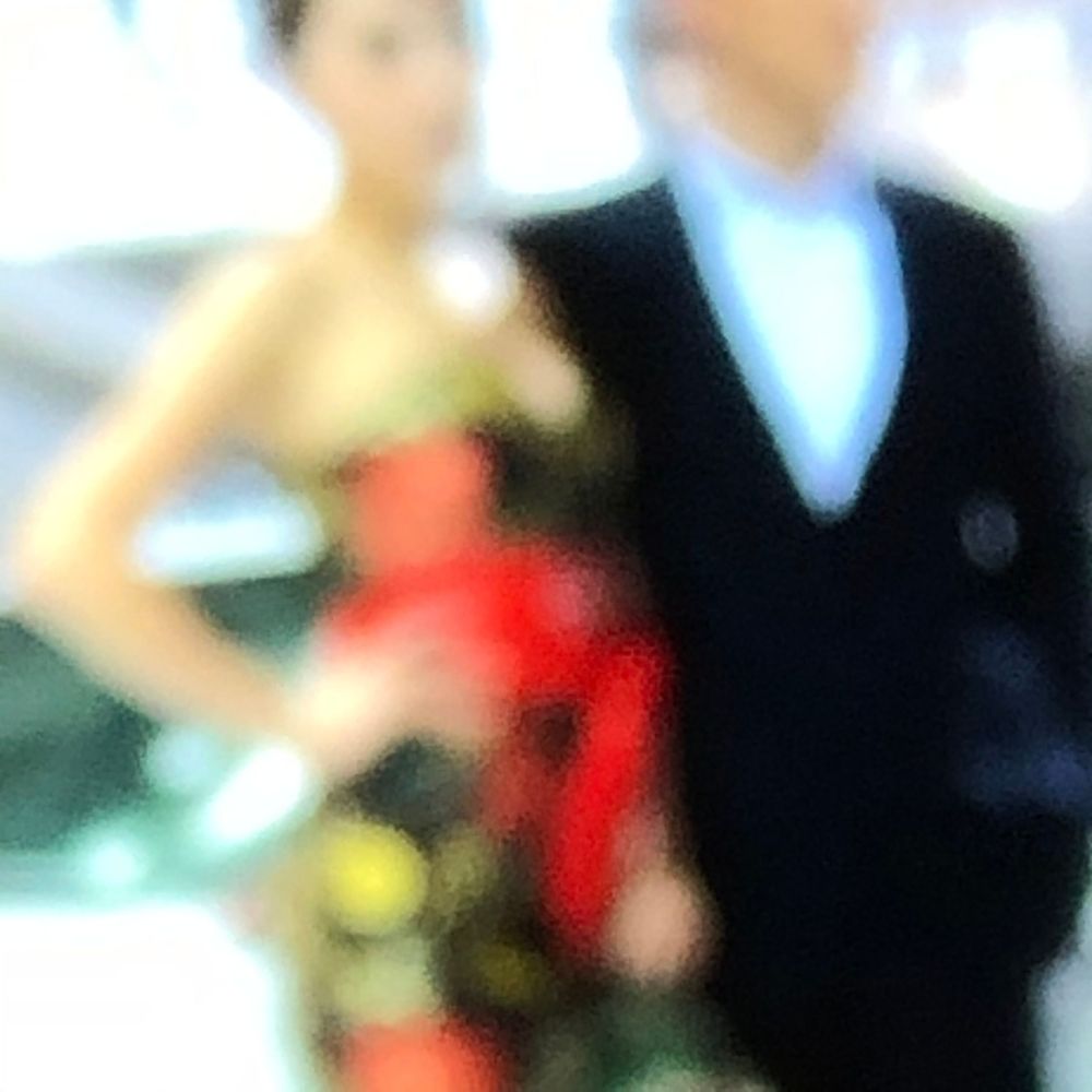 A blurry image of a woman in a colorful dress standing next to a man in a dark suit.