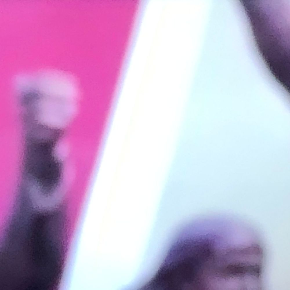 Blurry close-up image showing figures against a bright pink and white background with motion blur effect.